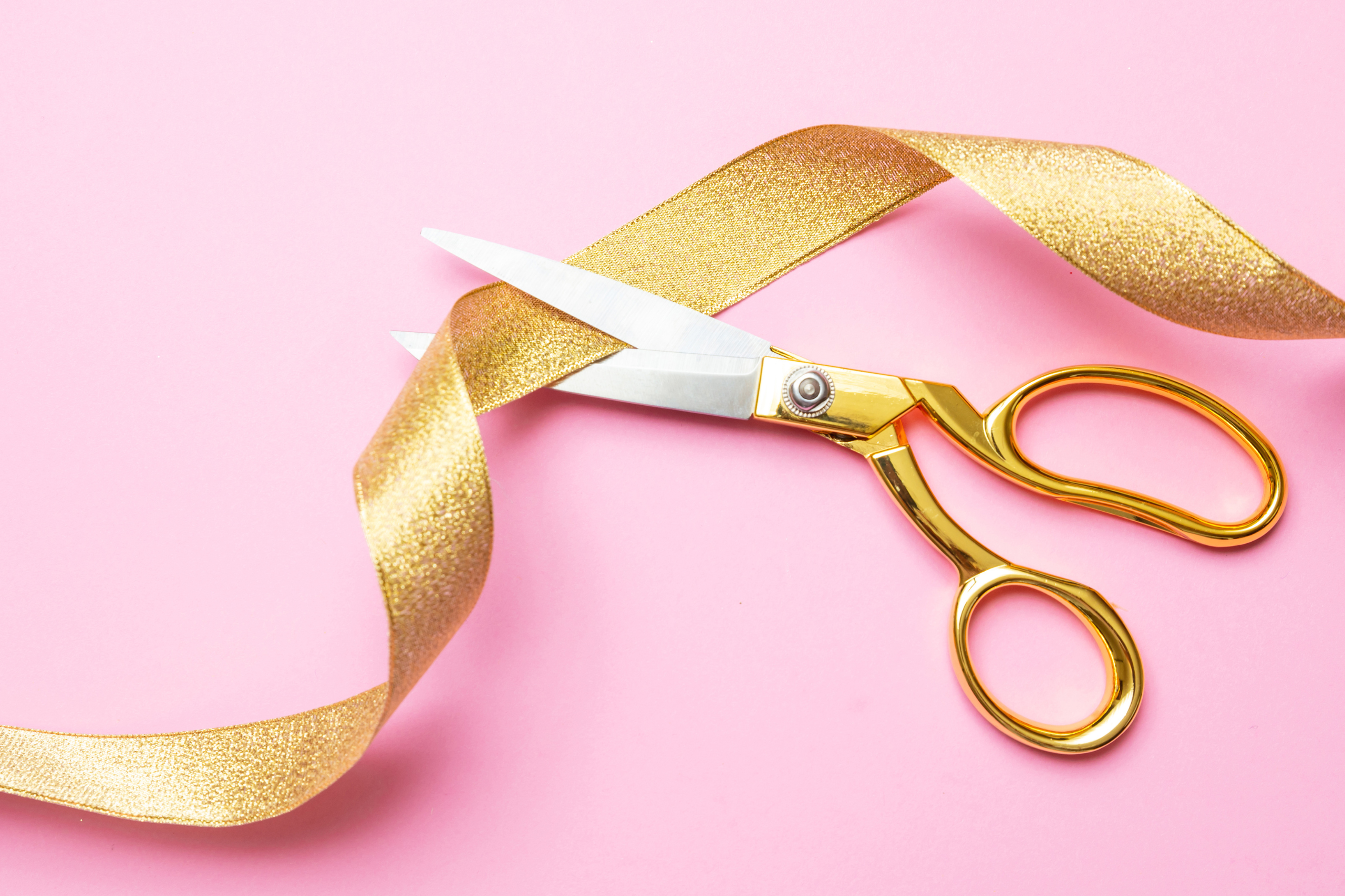 A gold pair of scissors is positioned to cut a gold ribbon.