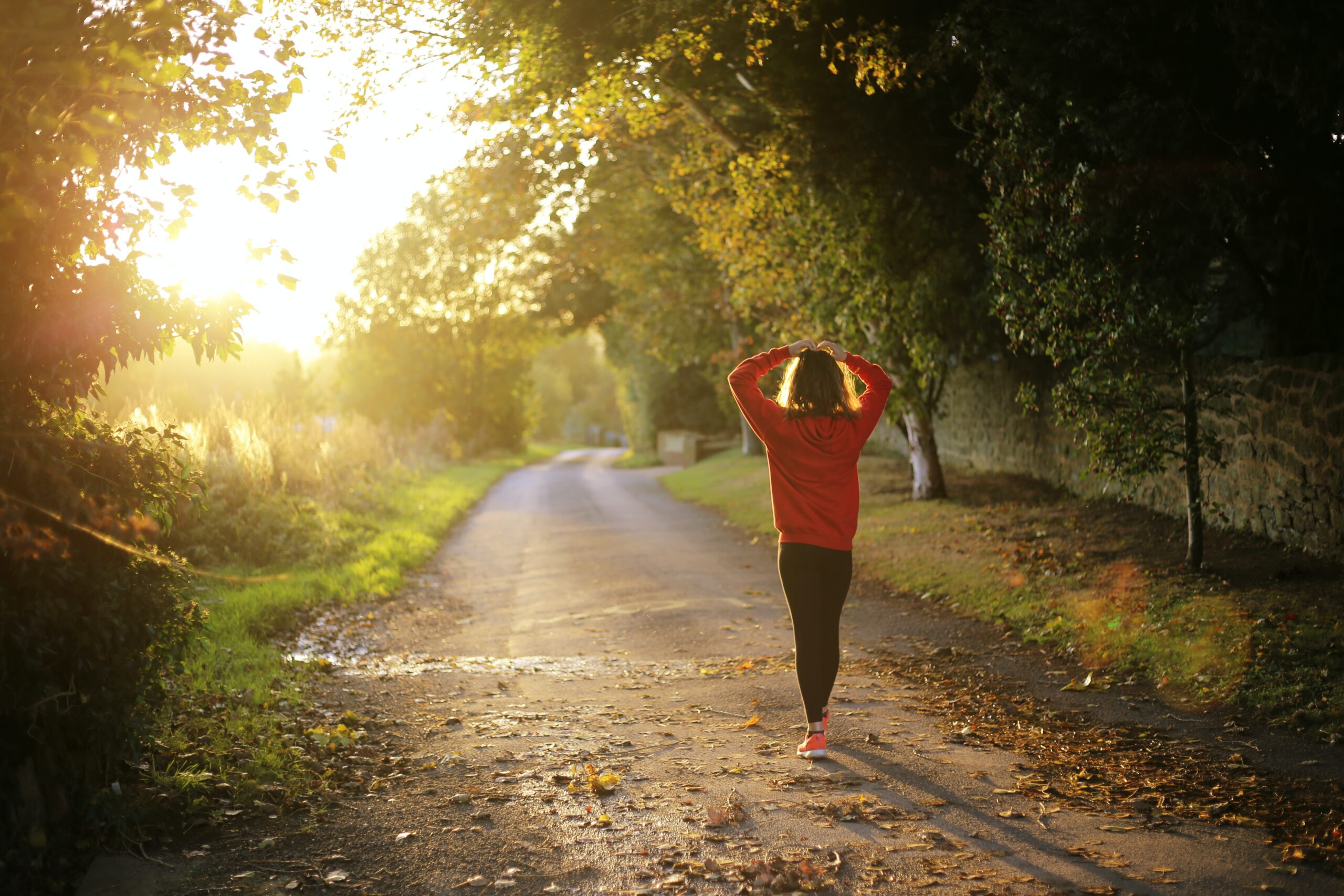 A woman walking through a wooded pathway with her hands atop her head.