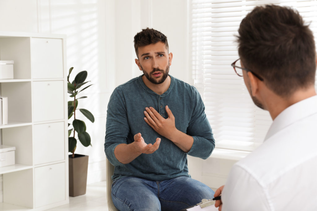 A man speaks passionately with his hand on his chest to another man with a white coat and clipboard.