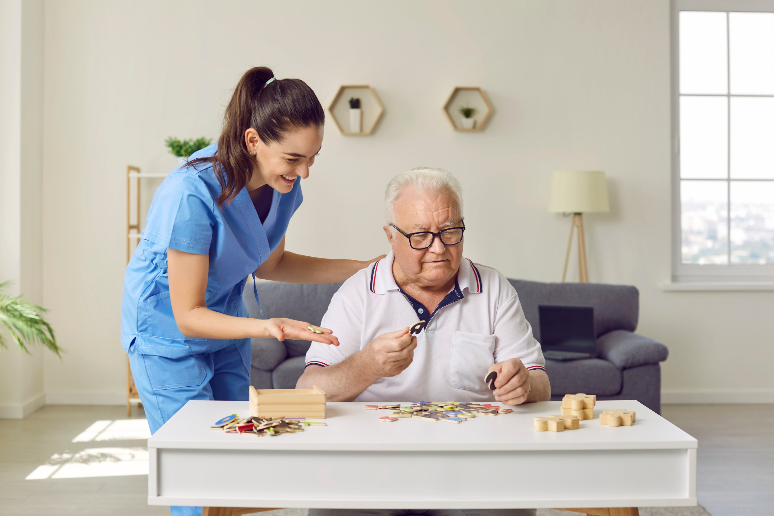An aide assists an elderly man in completing a puzzle.