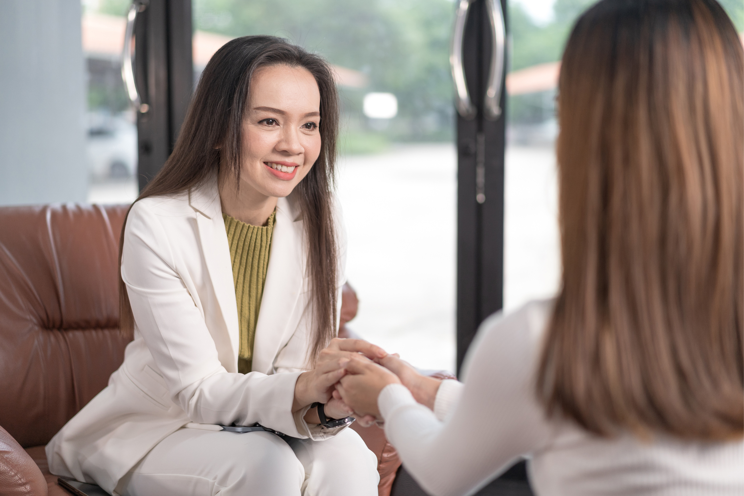 A therapist holds the hands of a client as they sit across from one another.