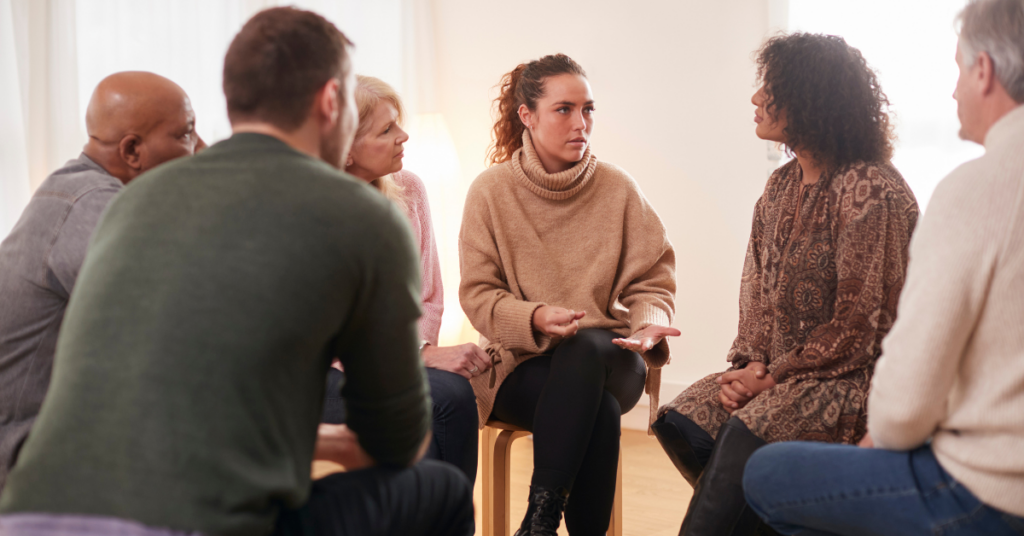 A woman speaks candidly while sitting in a circle of people who listen to her.