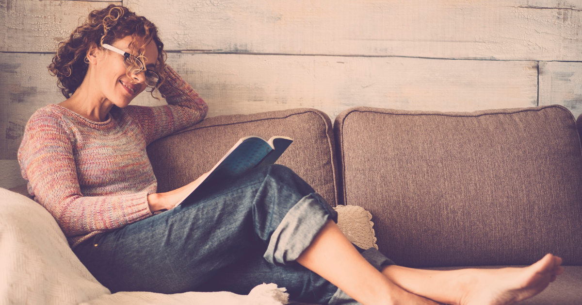 A woman sits on a couch reading a book.