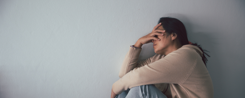 Depressed woman sitting on the floor with her knees bent and her hand on her face