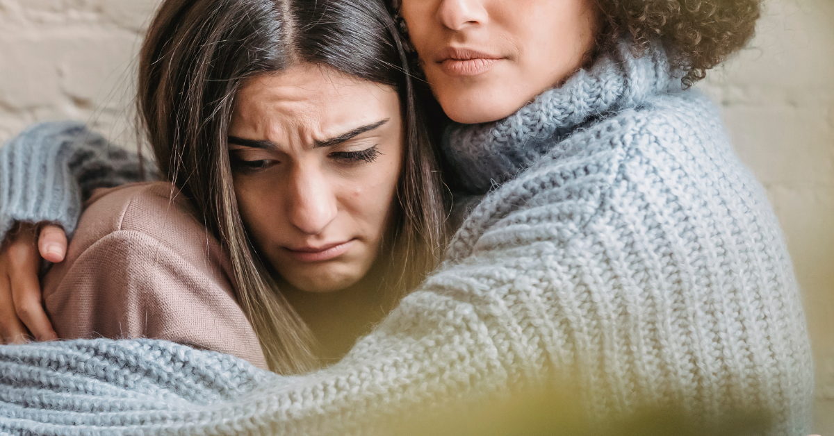 A woman looks sad while another embraces her.