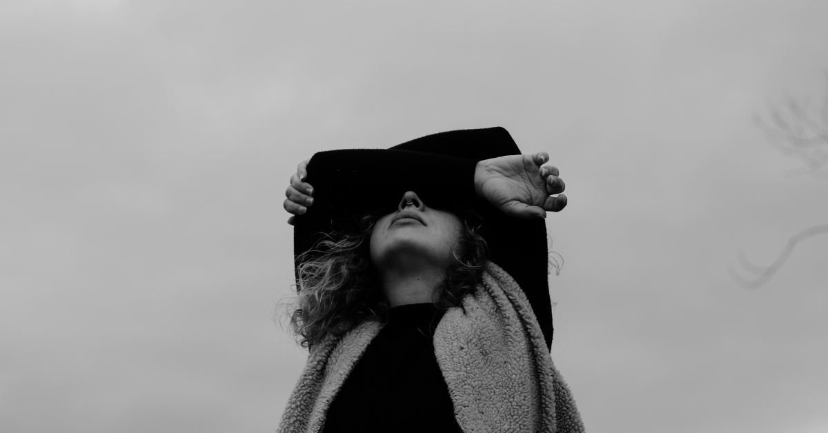 Gray image of a woman looking up toward the sky with her arms covering her eyes.