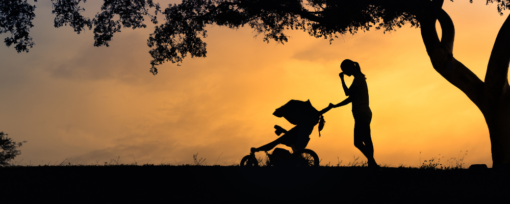 Silhouette of woman with a stroller against a sunlit backdrop.