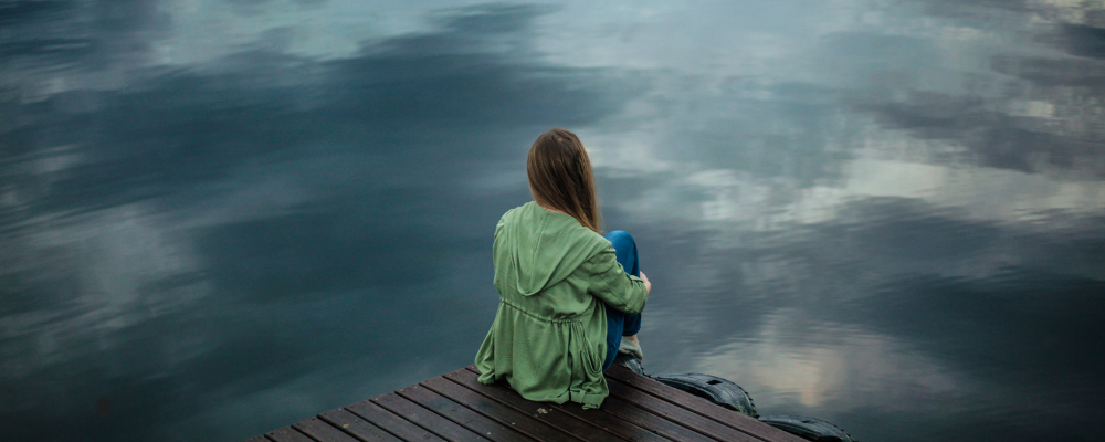 A woman looks longingly out toward a body of water sitting on a dock.