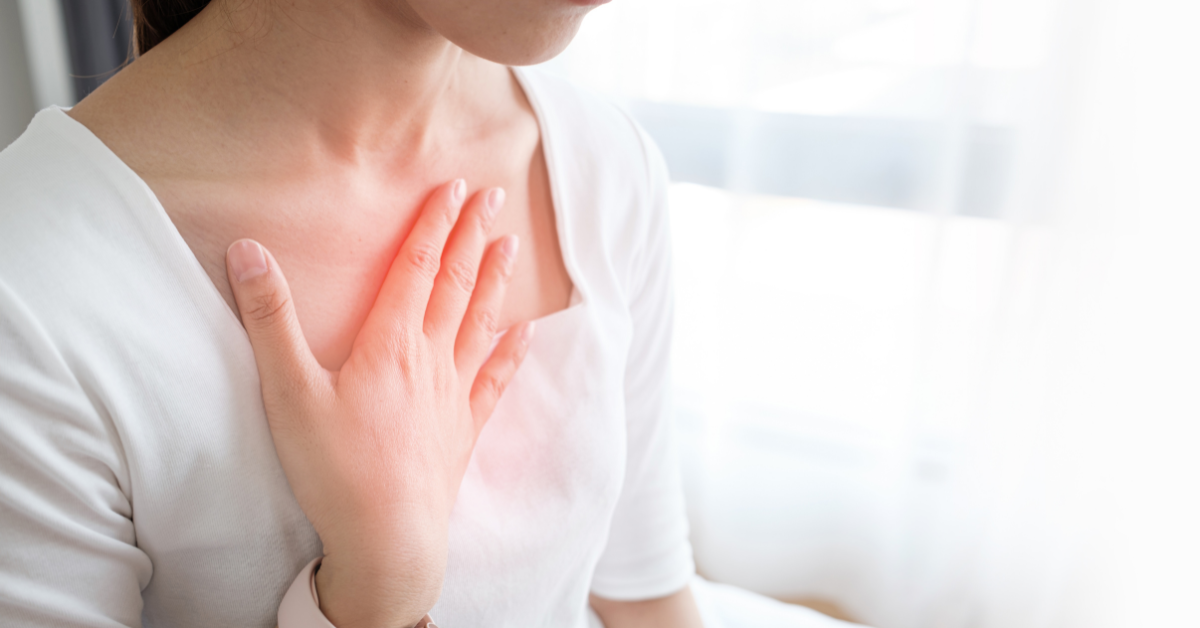 woman in a white top with her hand on her chest