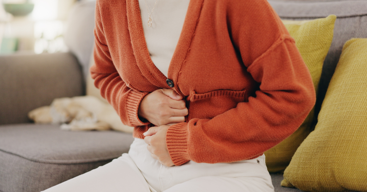 Woman in an orange cardigan holding her stomach with discomfort