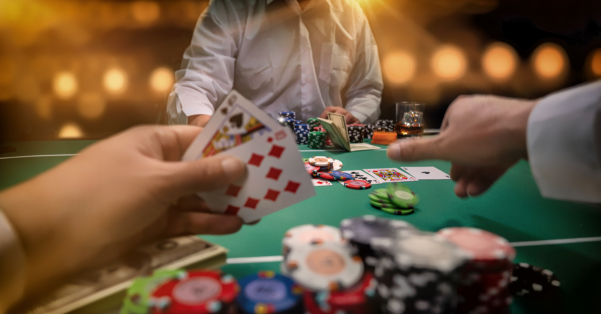 A close-up of a poker game, showing a player's hand holding two cards (one face-up, showing a Jack of Spades) and a stack of poker chips on the table. Another hand is visible, pointing at the cards.