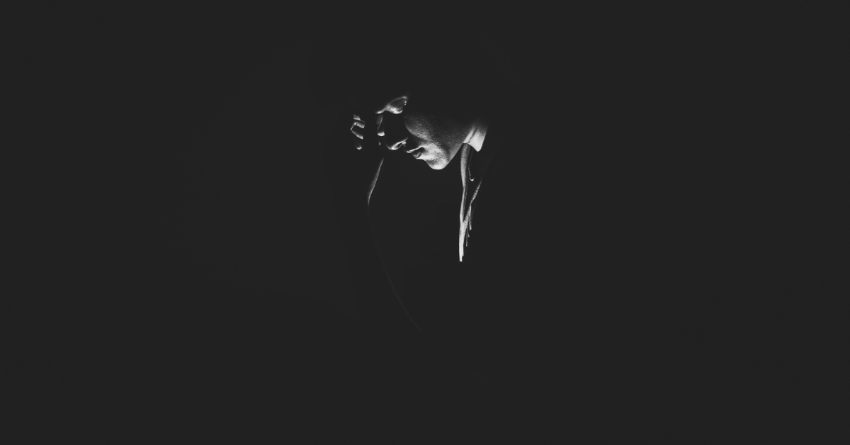 A person with their head in their hand, looking down, in a dark room.