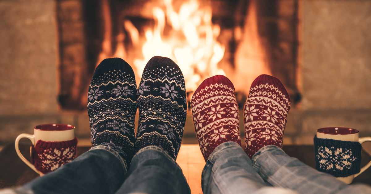 Two sets of feet with holiday socks on a table in front of a fireplace