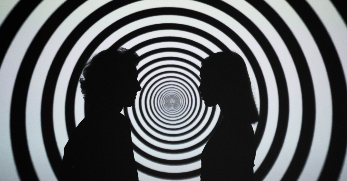Two silhouettes face each other in front of a hypnotic spiral background that draws the eye toward the center.