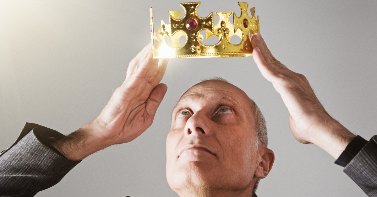 A man stares at a plastic crown he is holding above his head.