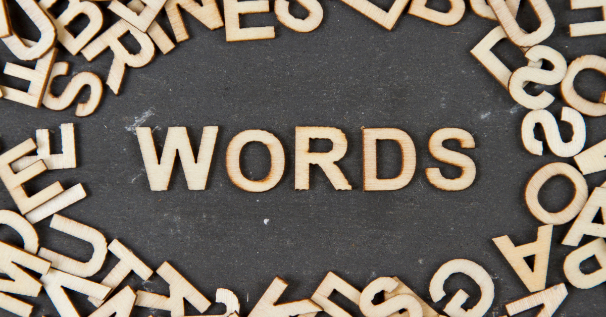 The word "WORDS" is spelled out in wooden letters, surrounded by scattered wooden alphabet letters on a dark surface.