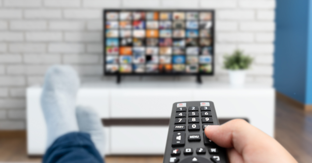 Person holding a remote while watching a television screen filled with show thumbnails, representing how fictional characters with mental disorders are portrayed in media.