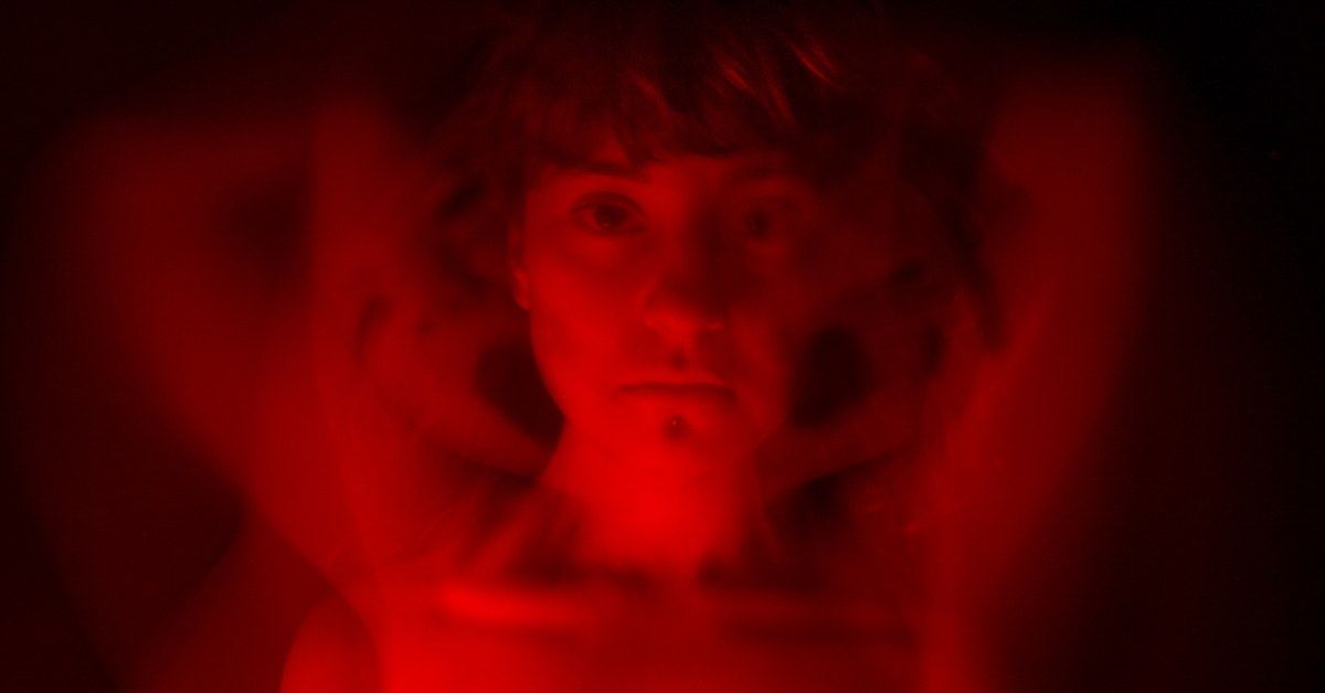 Ominous red-lit image of a woman staring directly at the camera.