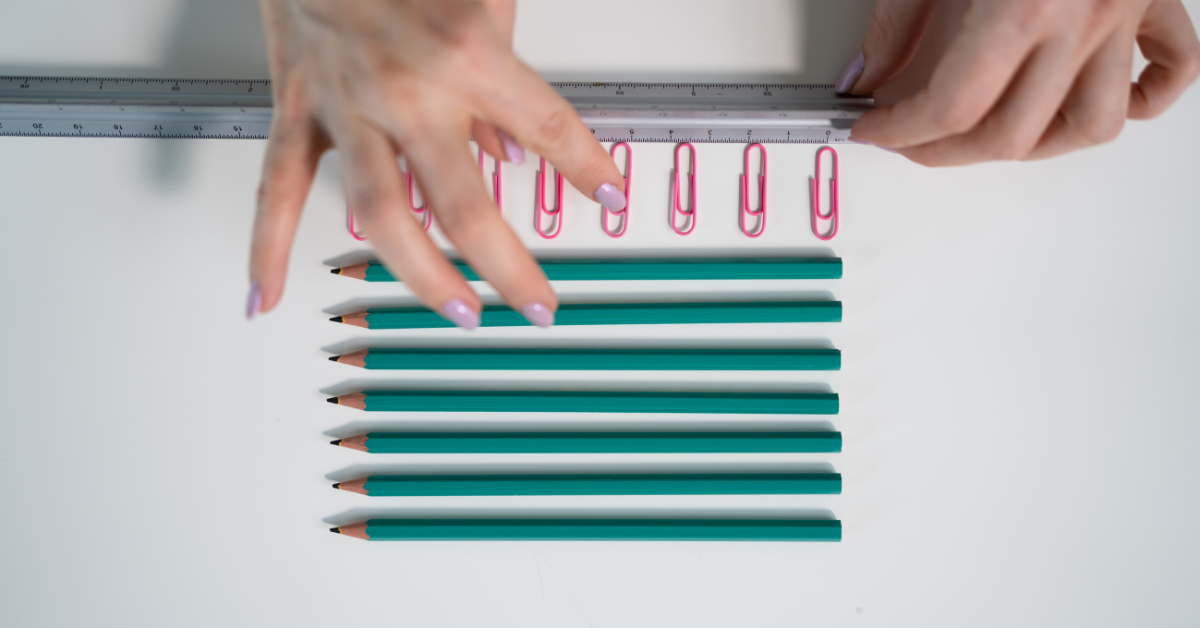Hands carefully organizing paperclips and pencils with a ruler.