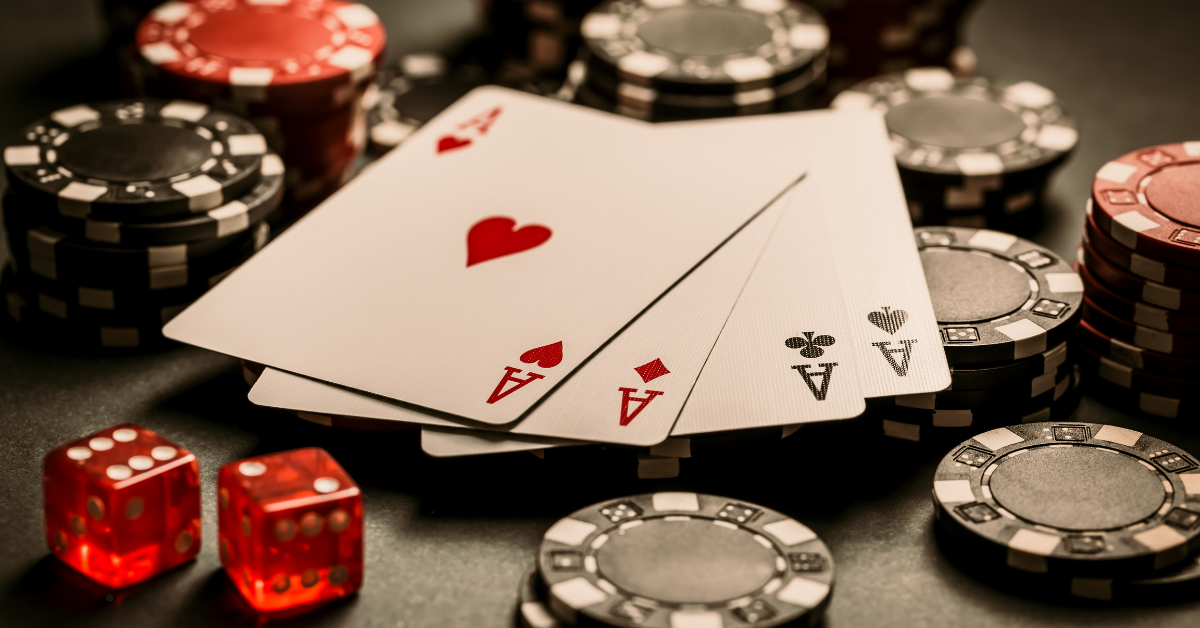 A close-up of poker chips, red dice, and a winning hand of four aces on a dark casino table.