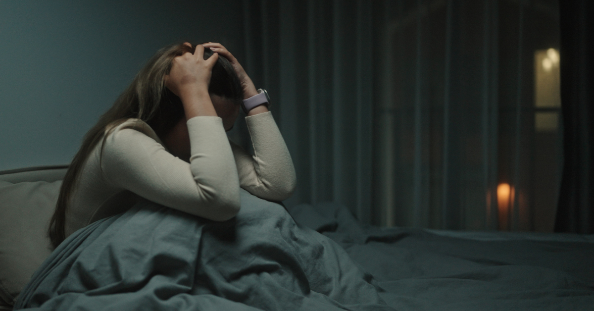 A woman sits up in bed at night, holding her head in distress, representing the impact of anxiety and the need for accessible online treatment options.
