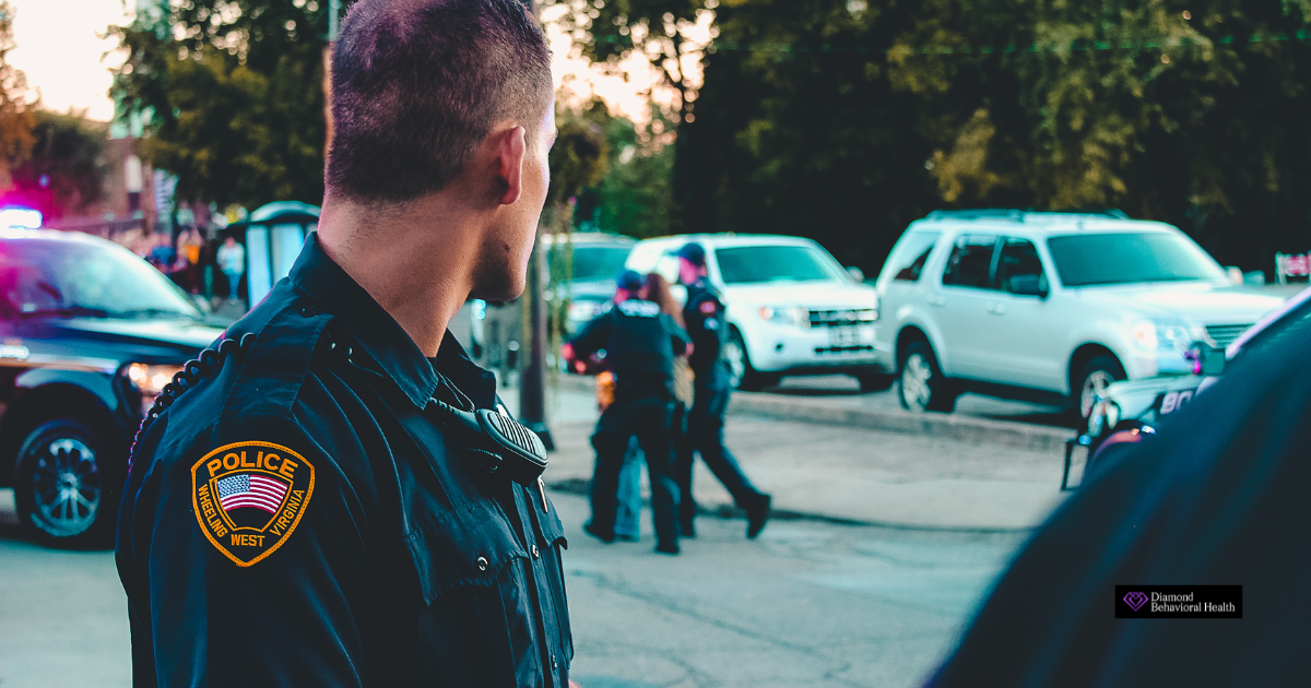 Police officer in uniform at a scene with multiple patrol cars and officers in the background, representing the growing awareness of mental health challenges in law enforcement