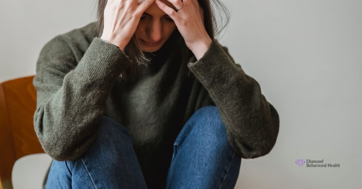 A woman sits with her head in her hands, showing signs of emotional distress. The image represents the emotional weight often linked to hereditary anxiety.