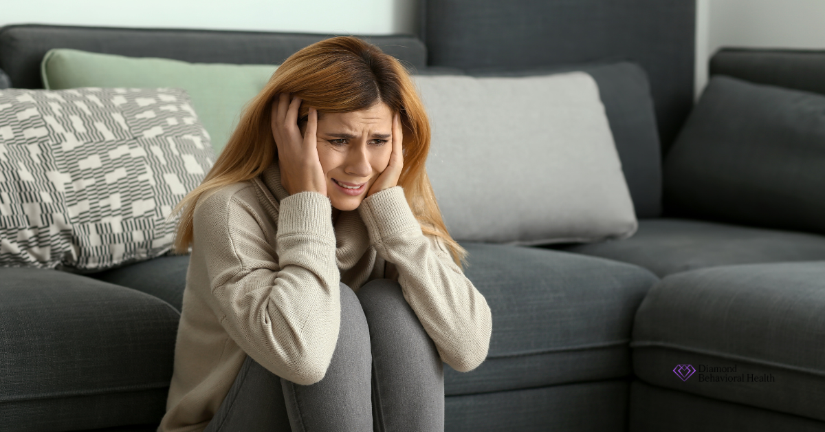 An anxious young woman sitting on the floor clutching her head, visually representing the emotional distress associated with the early stages of psychosis.