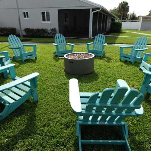 9 blue lawn chairs are positioned in a circle around a fire pit.